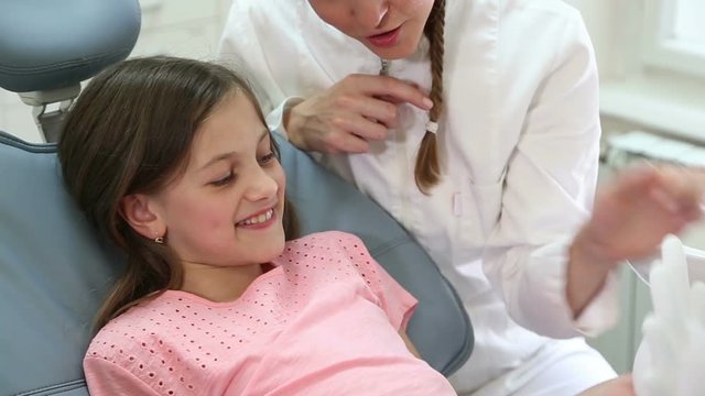 Close up of pretty girl and beautiful female dentist having fun playing with rubber glove