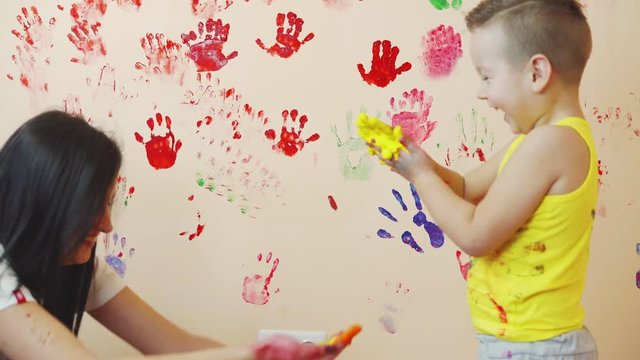 Happy mother and her cute boy having fun together leaving their colorful handprints on the wall. Young happy family. Mother and child concept