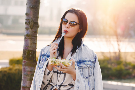 Young brunette caucasian woman eating fresh salad outdoor