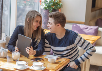 Cheerful couple dating in a cafe. They are having fun and smiling with tablet.  they are looking at each other