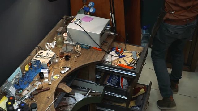 Jeweler gets up from the table with tools and goes to the grinding machine