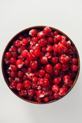 Above view on wooden bowl with frozen redcurrant on white background