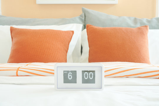 White alarm clock on bed with orange pillows in background