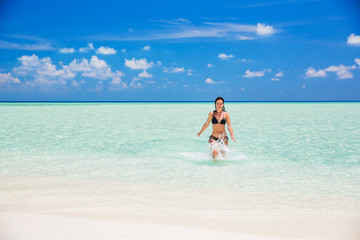 Attractive young woman enjoys Maldivian beach running in the ocean water