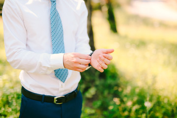 A man in a shirt and tie, puts his hand on the clock. Wedding groom accessories.