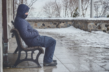 Man sitting on bench in winter with snow on the ground