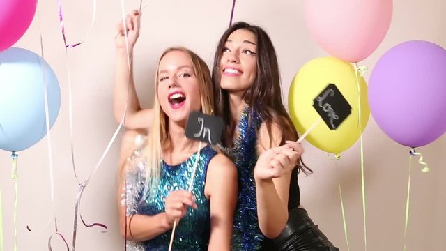 Cheerful female friends dancing with a sign in love in party photo booth 