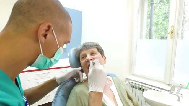 Elderly woman showing aching tooth to male dental surgeon