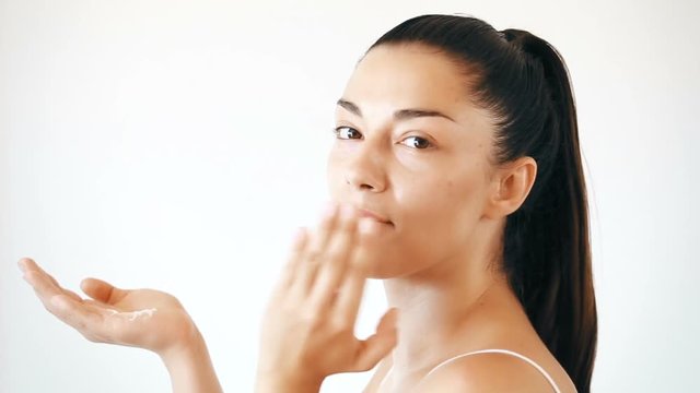 Profile of beautiful brunette woman applying cream on her face