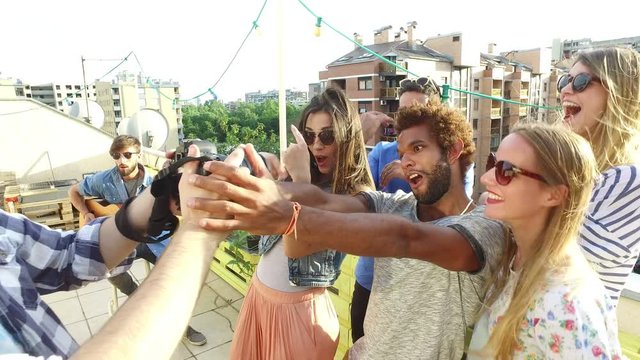 Group of smiling people taking photos while young musician playing guitar on the rooftop terrace