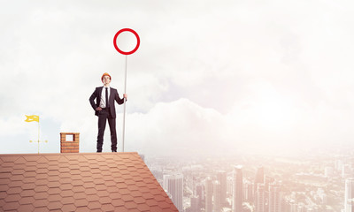 Caucasian businessman on brick house roof showing stop road sign