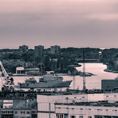 Military ship sailing past the cargo port in Riga, Latvia