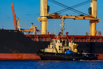 Black cargo ship mooring at the port with tug ship support