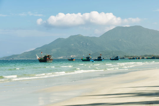Fishing boats in the vietnams port. Beautiful tropical beach, white sand, clear blue and green water, mountains  on background