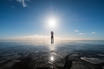 a man standing on frozen lake with sun and flare effects at winter