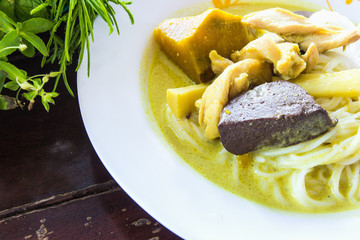 Green curry with meat on top of soft rice noodle on plate.