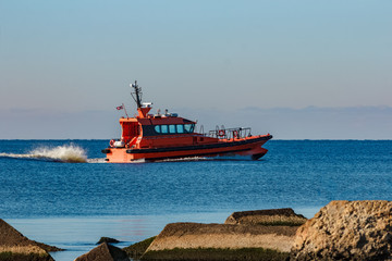 Red pilot ship moving at speed past the breakwater dam