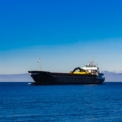 Obraz premium Black cargo ship with long reach excavator moving by baltic sea