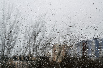 Fototapeta na wymiar Drops of rain on window in front of city buildings