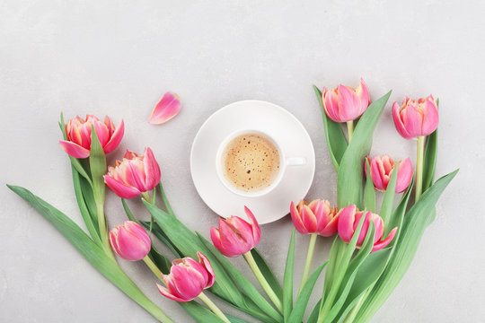 Cup of coffee with spring tulip flowers for good morning on gray stone table top view in flat lay style. Breakfast on Mothers or Womens day.