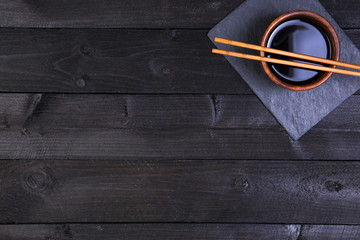 Fototapeta premium Sushi chopsticks and soy sauce on black background. Top view with copy space.