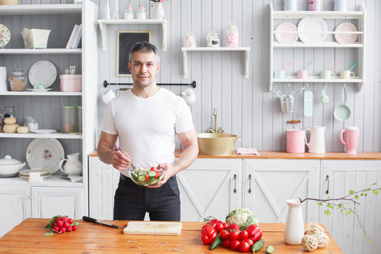 Middle-aged athlete, holding a bowl of a plate with a prepared salad of cucumber and tomato. - Powered by Adobe
