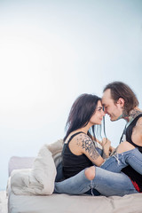 beautiful couple in white bed, brunette in a black shirt and jeans in the blanket, pressed against each other the sofa bed a couple of tattoos on a blue background copyspace