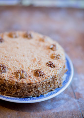 round delicious honey cake in blue white plate on light brown wooden background with flour