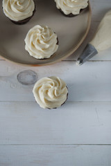 chocolate cupcakes white cream beige ceramic plate on white wooden table close-up top view