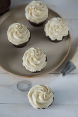 chocolate muffins and cupcakes white cream beige ceramic plate on white wooden table close-up top view