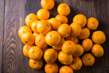 a bunch of sweet juicy delicious bright orange ripe Mandarin oranges are round lying loose on brown wooden backgroundб close-up