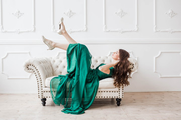 beautiful brunette girl in green dress lying on a white sofa looking at the camera