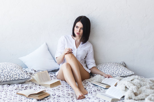 Cheerful teen girl sitting on floor among schoolbooks isolated on white