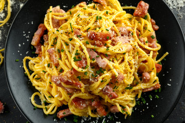 Classic Homemade Pasta carbonara Italian with Bacon, eggs, Parmesan Cheese on black plate.