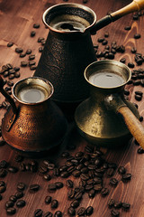 Hot coffee in group shabby antique turkish pots cezve with crema, beans with blur on brown old wooden board background, vertical shot. Rustic style.