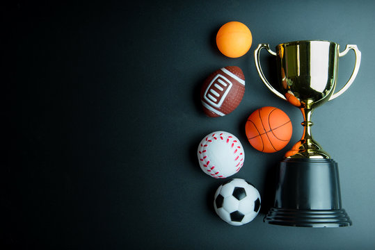 Golden trophy, Football toy, Baseball toy, Ping pong ball, Basketball toy and Rugby toy isolated on black background with copy space.Concept winner of the sport.