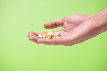 Colored pills in hand on green background.