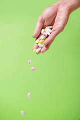 Colored pills falling from hand on green background.