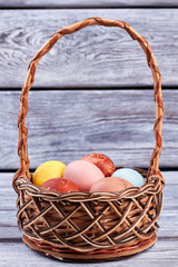 Easter basket with eggs. Wicker basket, gray wooden surface.