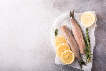 Freshly salted herring with salt, lemon ans rosemary on gray background with copy space. Traditional Dutch delicacy. Retro style toned. Top view.