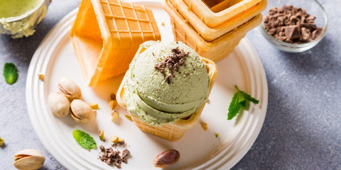 Pistachio ice cream with grated chocolate in waffle cups on gray stone background. Homemade summer food concept. High angle view