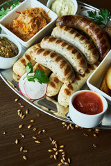 set of appetizers: grilled sausages grilled with slices of baked potato with stewed sauerkraut and grainy mustard and ketchup on wooden dark background