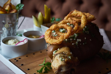 set of appetizers: roast pork knuckle with garlic and onion rings in batter, fried slices of potatoes, cabbage, pickles and various sauces - mustard and mayonnaise with herbs