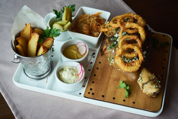 set of appetizers: roast pork knuckle with garlic and onion rings in batter, fried slices of potatoes, cabbage, pickles and various sauces - mustard and mayonnaise with herbs