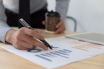 Businessman holding coffee cup and analyzing charts and graphs