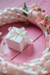 White gift box with white bow inside wreath with flowers on wooden pink background