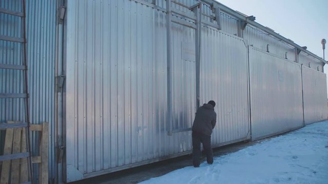 Production hangar for storage of wood products, laminated veneer lumber, and other products of the woodworking industry. Factory worker opens the door of the hangar to get the ready-made products.