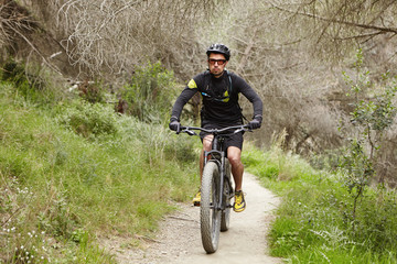 Fototapeta premium Confident professional rider preparing for cycling contest riding his electric bike, using pedal-assist system. Confident young European biker enjoying freeride outdoors in woods in the morning