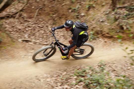 Motion picture of young Caucasian professional rider in helmet, glasses and sportswear speeding down forest trail on booster bike duing intensive workout while preparing for cycling competition