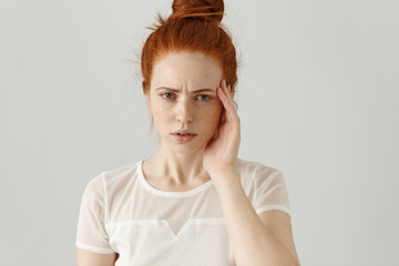 Unhappy stressed young redhead female with hair knot touching face while suffering from bad...